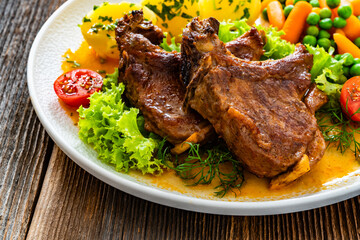 Baked veal chops, boiled potatoes, green peas and carrots on wooden table	