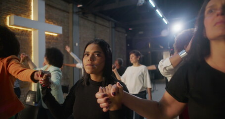 People holding hands during worship service, expressing unity and joy, illuminated cross symbolizing faith and community in a spiritual and uplifting environment