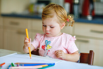 Cute adorable baby girl learning painting with pencils. Little toddler child drawing at home, using colorful felt tip pens. Healthy happy daughter experimenting with colors at home or nursery.
