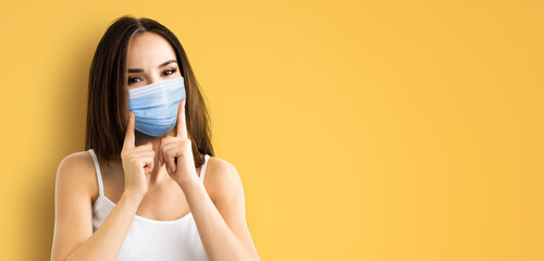 Coronavirus, pandemic, protective concept - brunette hair young woman wearing showing face protection medical mask, isolate orange yellow background. Free space sign text area