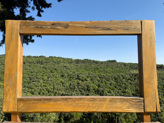 Travel photo spot with wooden frame overlooking vast green forest under blue sky, ideal for adventure blogs, tourism ads, scenic branding visuals