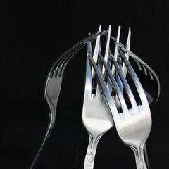 Close up view of kitchen forks hooked and supporting each other over black surface
