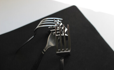 Identical forks from the same kitchen set are arranged in the shape of a tent on black napkin 
