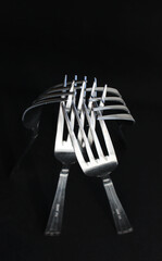 Intertwined prongs of shiny table forks on black background
