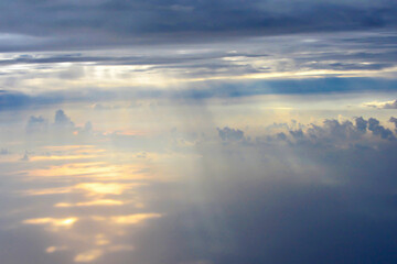 Sunlight breaking through dense clouds above ocean surface during flight. Clouds create dreamy...