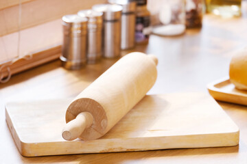 The rolling pin is placed on the wooden cutting board in the kitchen.