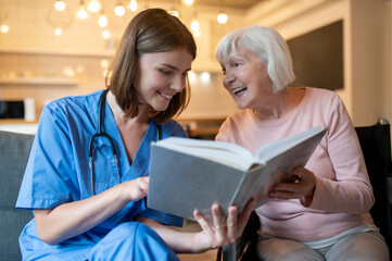 Female care assistant reading a book to a elderly lady and both looking enjoyed