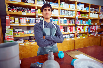 Young latin American hardware store employee wearing apron standing behind counter with plumbing supplies and clipboard