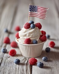 Paper cup filled with patriotic ice cream, topped with a mini American flag; placed on a wooden table with fresh raspberries and blueberries. 4th of July celebration concept