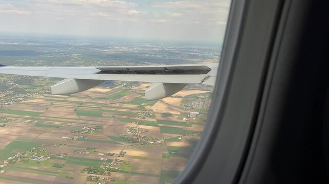 Plane wing above cultivated fields with view of scattered houses and distant city near Warsaw