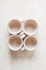 Handmade unglazed ceramic cups in natural clay color on beige background. Artisan pottery with organic texture and minimalist aesthetic. Slow living and modern rustic style