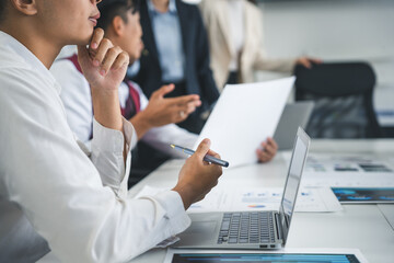 Businesspeople engaged in a meeting, analyzing graphs and statistics while utilizing laptops and reviewing various documents