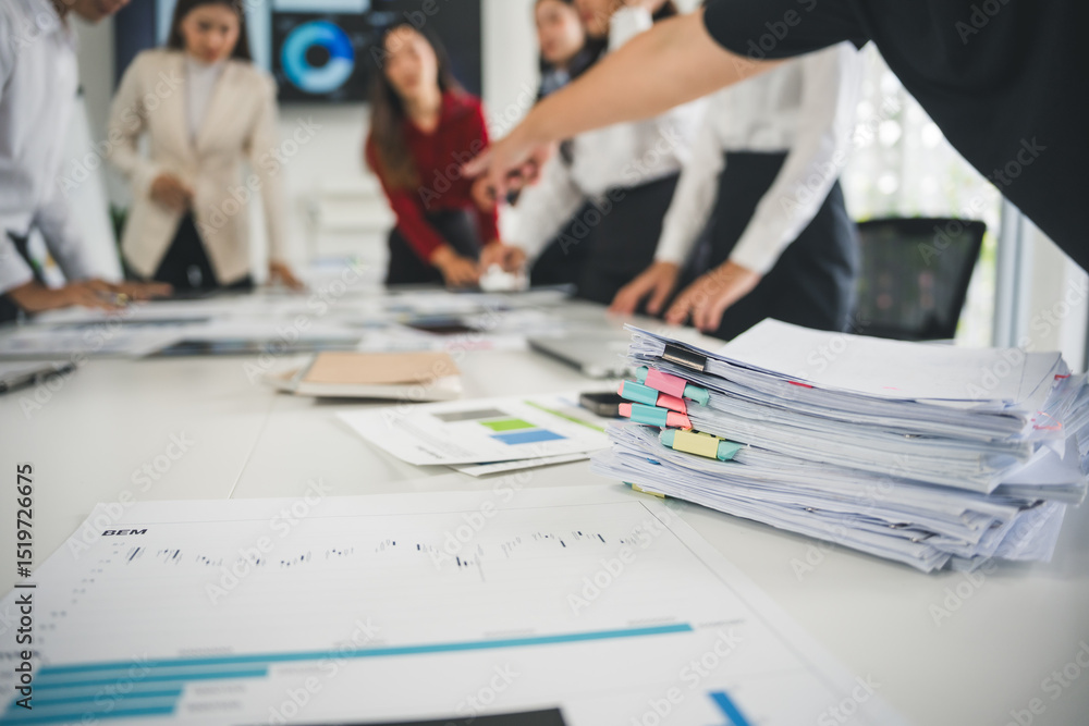 Poster stack of paperwork on a table with businesspeople analyzing financial charts during a meeting in a b