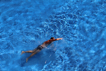 Man swimming in sporty crawl style against blue pool background, view from above (Tenerife, Spain)