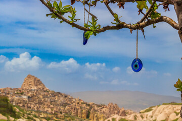 Landscape with blue Evil Eye pendants in Wish tree against blurred background of Uchisar castle in Cappadocia, Turkey. Selective focus