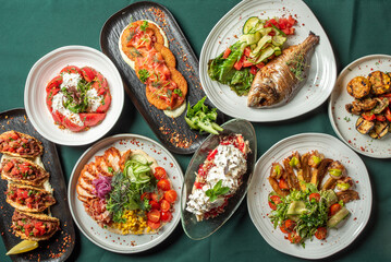 A colorful assortment of dishes on a green tablecloth, including grilled fish, tacos, salads, roasted vegetables, and a dessert with whipped cream. A vibrant and appetizing culinary display