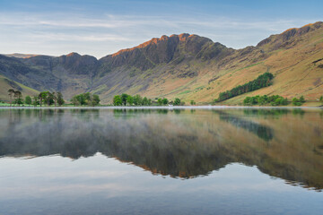 Morning reflections in calm lake at Buttermere in The Lake District National Park, UK.