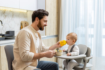 Father and a cute little baby boy having breakfast in the kitchen