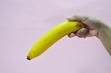 Hand holding banana fruit on pink  background, health illustration photo concept. Health photo concept. Health advertising photo concept. Male genital size illustration.

