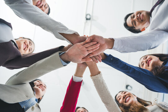 Group of smiling asian businesspeople joining hands together showing teamwork, unity and success in business