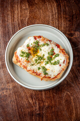 A delicious homemade pizza with melted mozzarella cheese, tomato sauce, and fresh parsley on a white plate, placed on a rustic wooden table. Perfectly baked, appetizing, and ready to enjoy