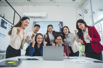 Group of Asian businesspeople celebrating success in an office meeting room, joyfully engaging with a laptop and sharing their achievements © Crystal