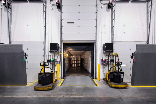 Interior of warehouse loading dock, with truck parked loading and two electric fork lifts on each side