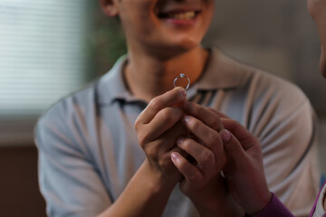 Smiling man presenting an engagement ring while proposing to his girlfriend, capturing a moment filled with love and joy indoors