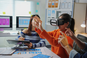 Asian UIUX web designers testing a virtual reality app in the office, wearing VR headsets and...