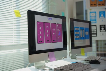 Desktop computer displaying mobile app design in a bright ux ui design studio with notes and...