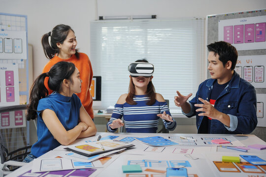 Team of Asian software developers collaborating in a modern office, testing a virtual reality app and refining user experience design