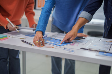 Ux designers collaborating on a new mobile app interface, actively pointing at a detailed wireframe...