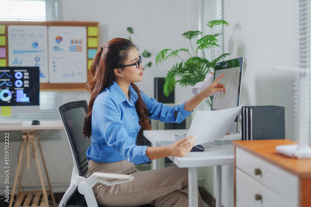 Poster businesswoman pointing at computer screen showing graphs and holding document with financial data, w
