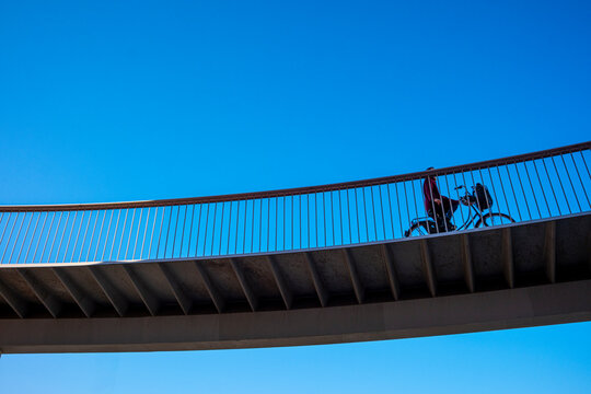 Cyclist crossing elevated urban bike lane under blue sky, captured from below in modern city infrastructure, ideal for clean transport and sustainability concepts.