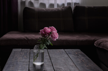Pink flowers roses in a transparent vase on an old wooden table in a brown room