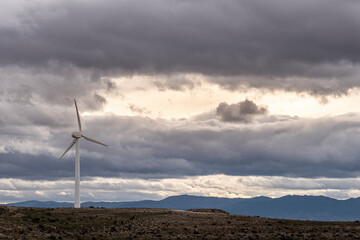 Wind turbine under heavy clouds in open field near Zaragoza, with environmental message and space for copy or branding use.