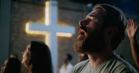 Bearded man singing and worshiping in church near illuminated cross, heartfelt expression of faith...