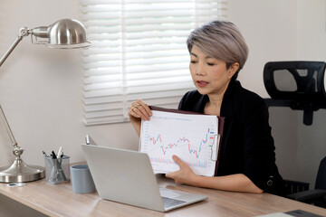 Elder Business woman is sitting at a desk with a laptop and a tablet