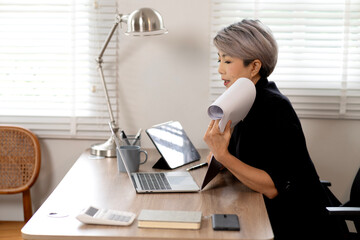 Elder Business woman is sitting at a desk with a laptop and a tablet