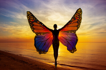 Graceful Woman with Vibrant Butterfly Wings on the Beach at Sunset Sunshine. Magical Mood of Transformation. Healing Meditation. Rear View of Girl Silhouette with Open Arms at Colorful Sea Sky view