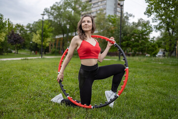 A girl in a red tank top and sweatpants does exercises and acrobatic tricks with a hula hoop on a...