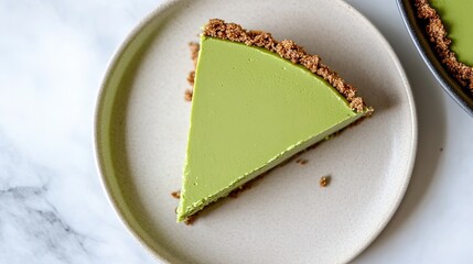 Top-down view of a matcha cheesecake slice on a neutral-colored plate, placed on a smooth, empty surface. 