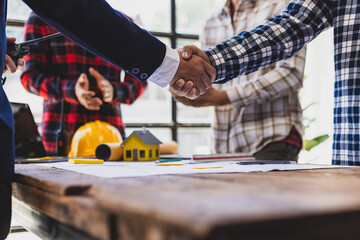 Architect and construction worker shake hands during meeting over house project, collaborating in office meeting. Team discusses blueprint for new home, emphasizing teamwork in real estate industry.