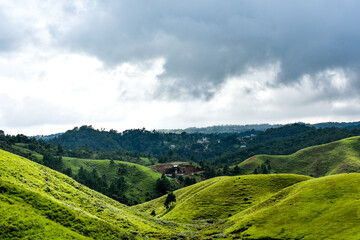 Rolling green hills and dense forests stretch towards a cloudy sky, showing rural landscape of...
