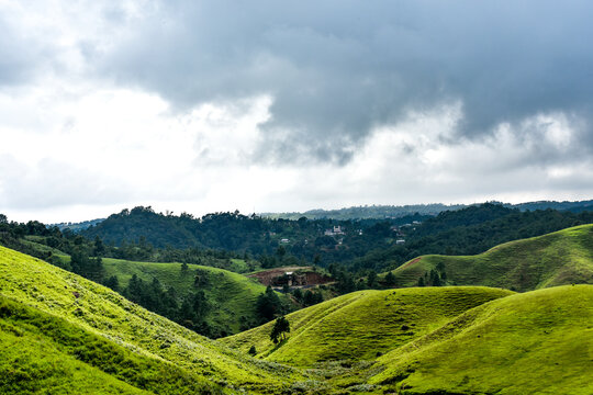 Rolling green hills and dense forests stretch towards a cloudy sky, showing rural landscape of Mawlangkhar, Meghalaya.