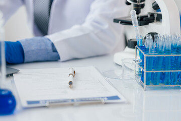 Scientist taking notes during experiment in laboratory. The lab table is filled with test tubes, beakers, and a microscope.