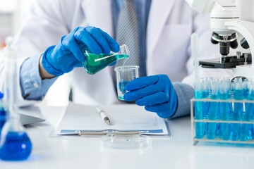 Scientist analyzing liquid in laboratory setting. Scientist is holding a conical flask with a blue liquid, conducting research in a laboratory equipped with a microscope and test tubes.