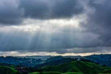 Dramatic light ray piercing dark clouds over the rolling green hills of Mawlangkhar, Meghalaya.
