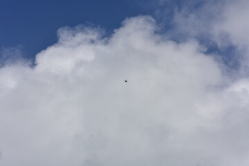 A lone drone flies high in a vibrant blue sky, partially obscured by white clouds.