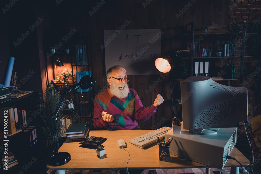 Poster elderly male programmer working on computer in home office illuminated by warm light